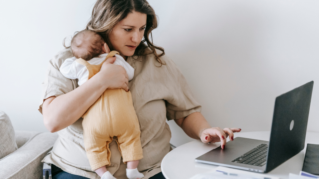 mom holding baby working on laptop